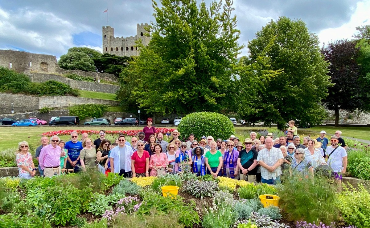 A large group of supporters posing amid the sensory garden with trees and Rochester Castle keep in the background