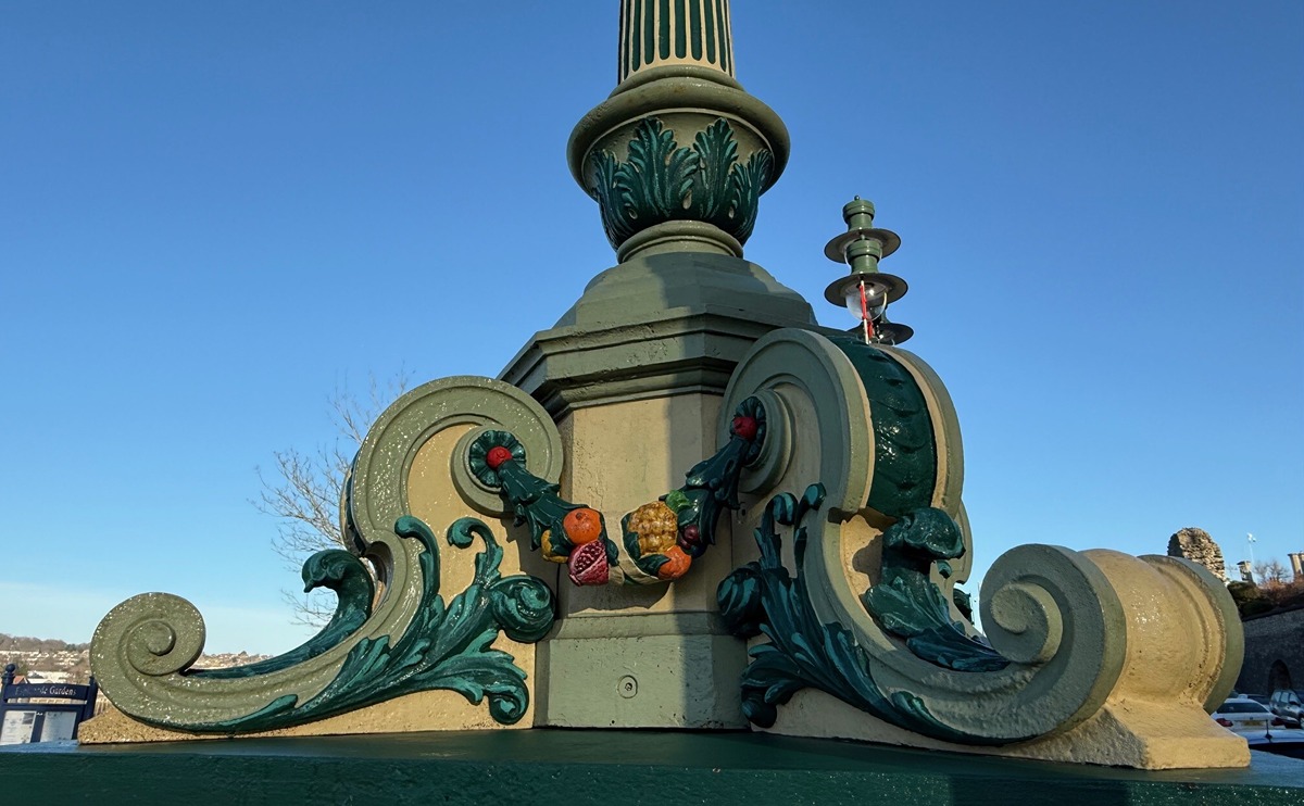 A detail photograph of the base of the ornate iron lamps that frame the northernmost entrance to the Esplanade Gardens