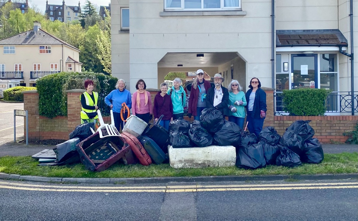 A group of volunteers stand in front of about 15 black bags of collected litter and some other larger items taken from the foreshore