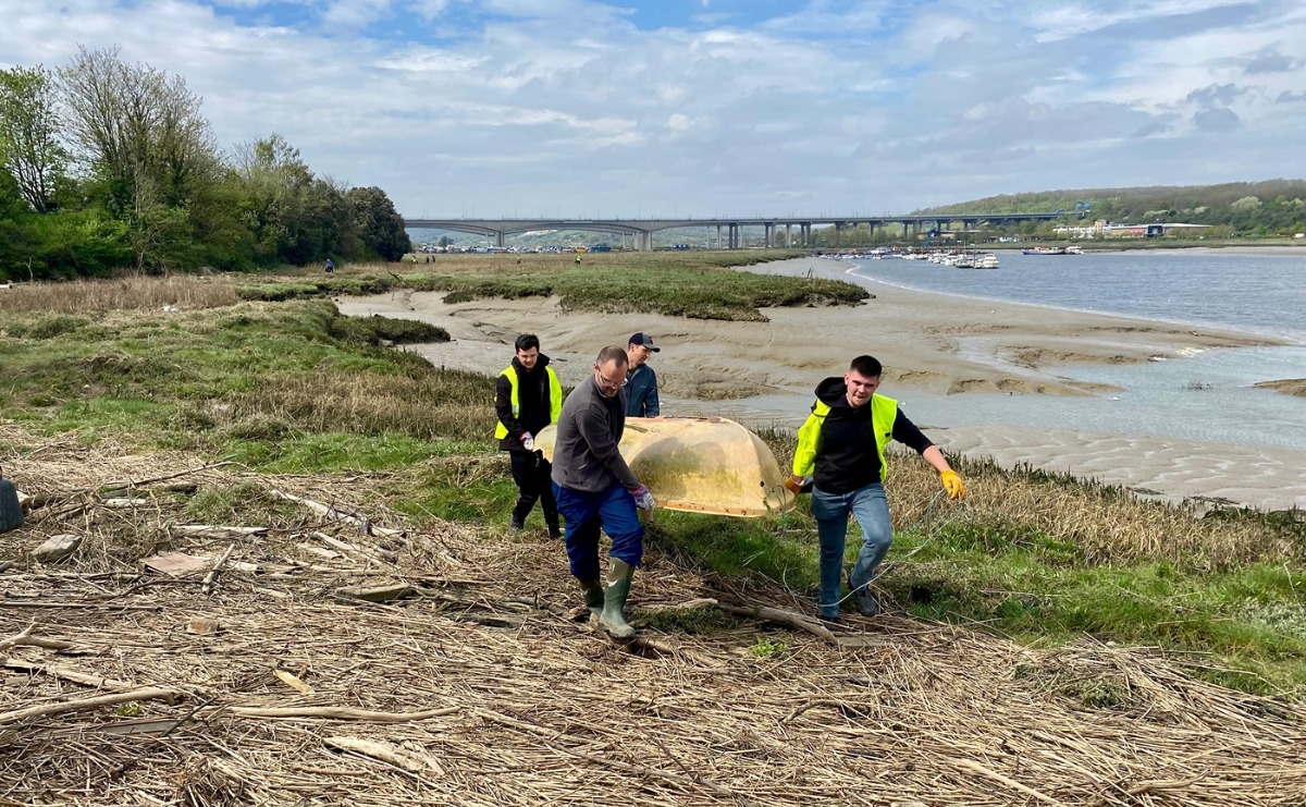 Volunteers carry a fibreglass dinghy, rather the worse for wear, up from the foreshore